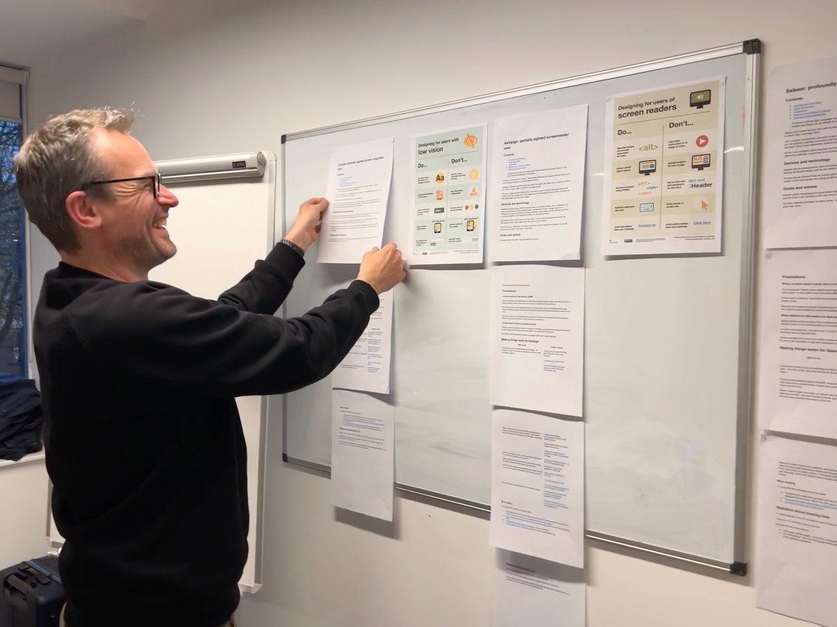 Alistair Duggin sticking do’s and don’ts for accessibility on a wall.  He’s smiling.
